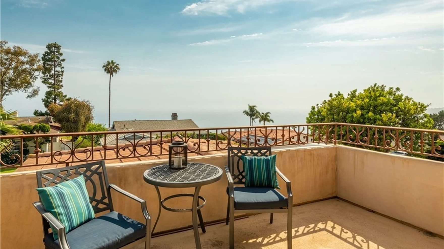 Original upper terrace behind a solid stucco parapet with a tiled floor and a wrought-iron patio set, ocean visible over the wall