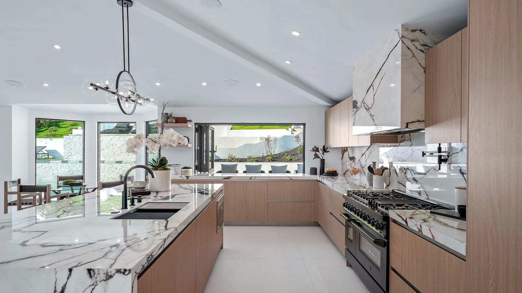 Rebuilt kitchen: an island in mirrored stone with the veining carried down both ends, black seating, oak fronts, appliances built in flush and a pro range
