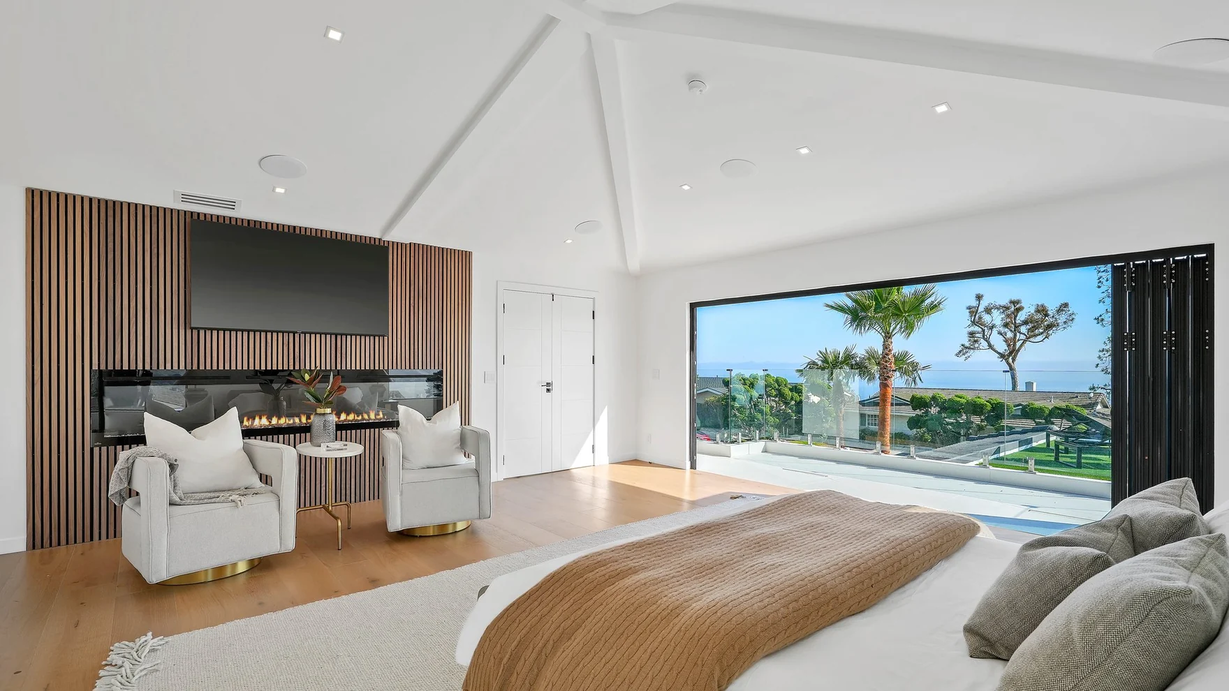 The same room now: battened timber running floor to ceiling behind the bed, pale board underfoot, and glazing that opens onto a deck above the water
