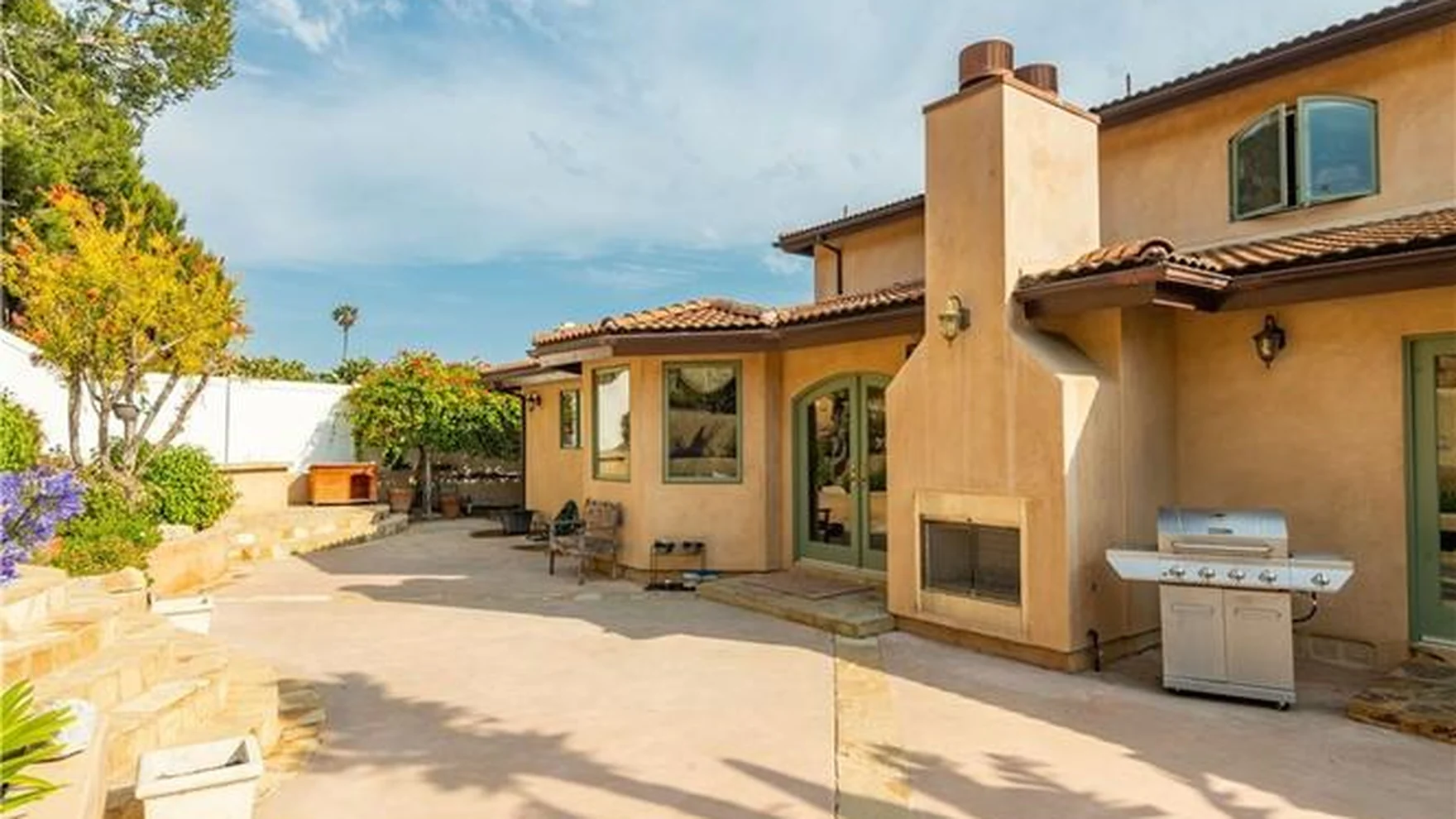 Garden side as found: rendered walls, curved clay roof tiles, a rendered chimney breast, a masonry grill counter and clay-tiled paving
