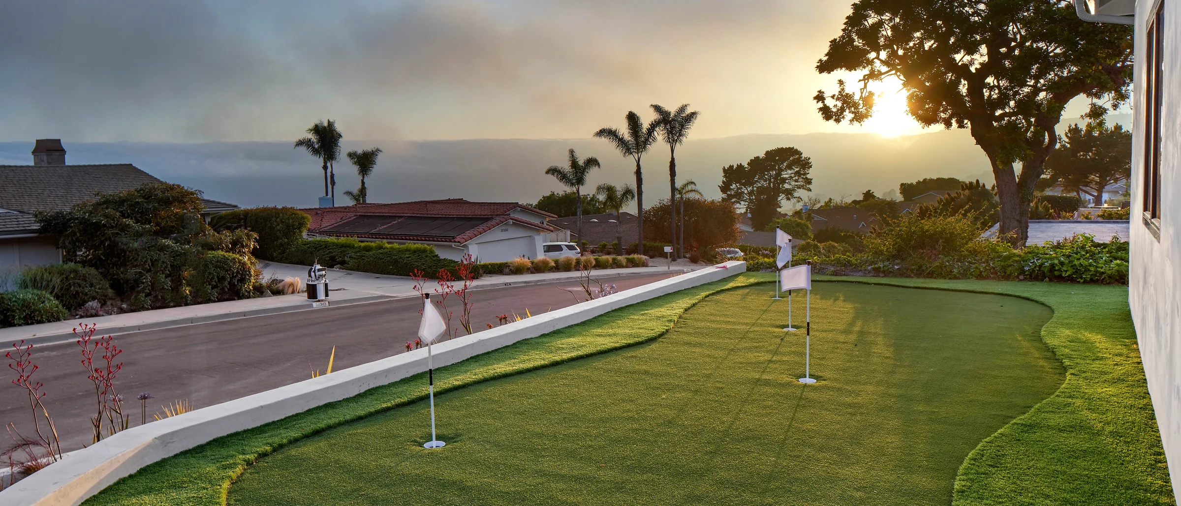 Putting green at low sun with the coastline behind the rebuilt house