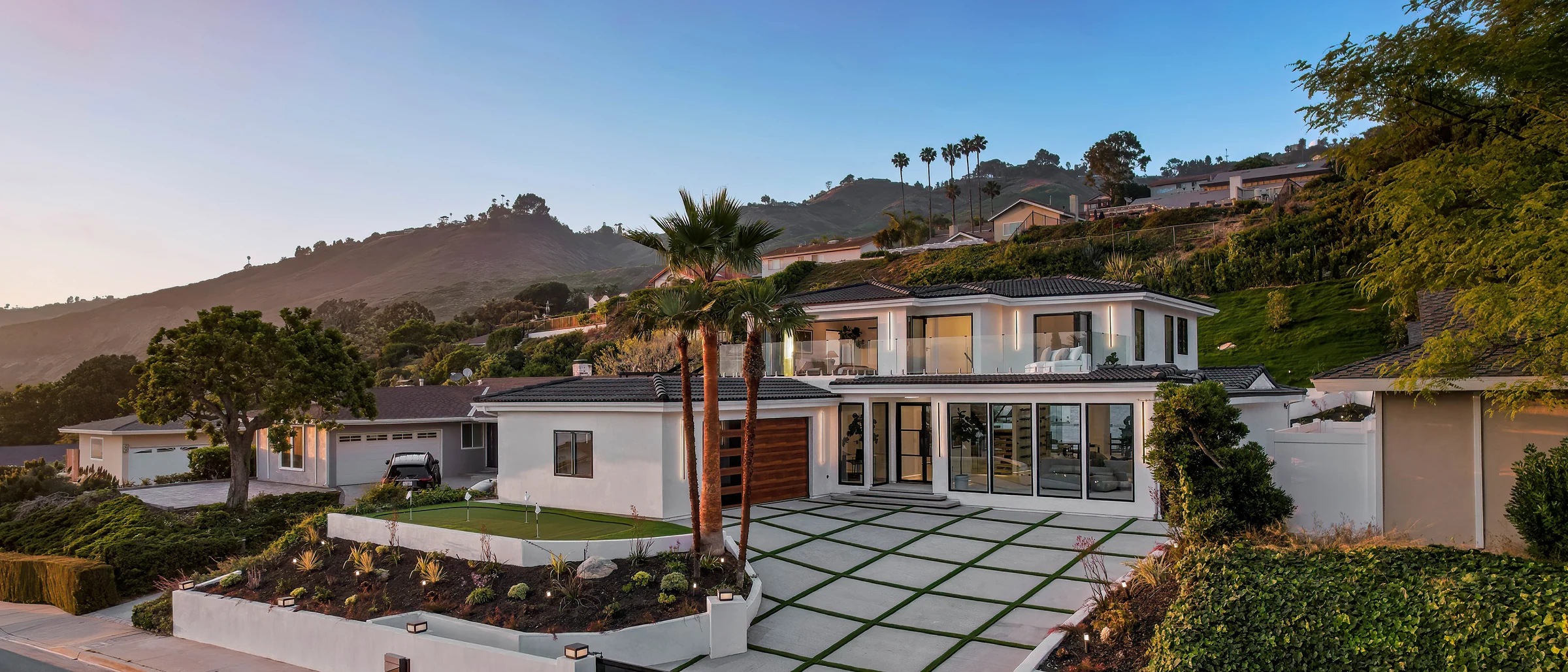 Wide view of the rebuilt modern front elevation at twilight with a low roofline and glowing glass